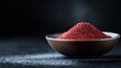 © Maximages  - A rustic bowl filled with vibrant red spice sits on a dark backdrop, casting a captivating contrast. Fine grains are scattered outside the bowl, enhancing texture.