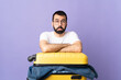 © luismolinero - Traveler caucasian man with a suitcase full of clothes over isolated purple background with sad expression