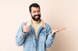 © luismolinero - Caucasian man with beard over isolated background holding copyspace imaginary on the palm to insert an ad and with thumbs up