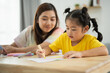 © WMSTUDIO - A young girl is drawing with a marker on a piece of paper while her mother watches. Concept of bonding and learning
