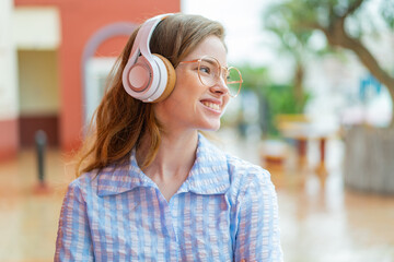 Wall Mural - Young redhead girl headphones at outdoors happy and smiling