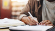 © LuxeShutter24/peopleimages.com - Hands, writing and books with person in library for knowledge, education and college thesis. Academy, future and university with student and studying on campus for exam, project and scholarship