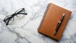 © Kukar Studio - A brown leather bound spiral notebook and a pair of spectacles on a white marbled surface, ready for writing and contemplation