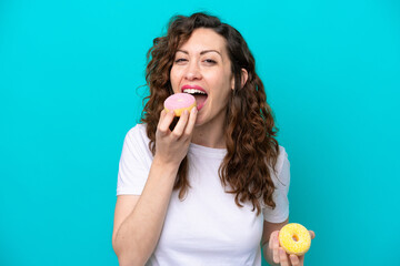 Wall Mural - Young caucasian woman isolated on blue background eating a donut