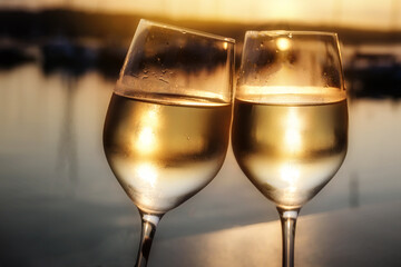 Two glasses of wine toasting at sunset on the shore in front of calm water, romance on a beautiful summer evening during the vacations, copy space