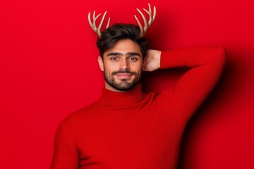 Wall Mural - Man wearing red sweater with white and brown patterns. He is wearing a pair of antlers on his head. andsome man in his thirties wearing deer antlers and a red Christmas sweater, red color background,