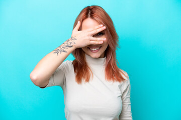 Young Russian woman isolated on blue background covering eyes by hands and smiling