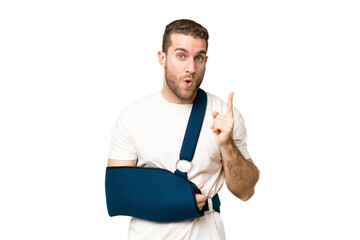 Sticker - Young handsome blonde man with broken arm and wearing a sling over isolated chroma key background intending to realizes the solution while lifting a finger up