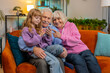 © Andrii Iemelianenko - Little Caucasian girl teaching grandfather and grandmother using smartphone on sofa in living room. Grandparents watching granddaughter play games on mobile phone. Happy family at home during weekend.