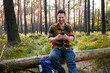 © baranq - Happy man using mobile phone sitting in forest during weekend hike trip