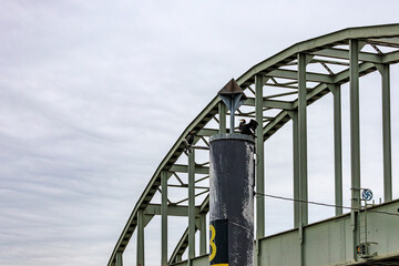 Close-up of arched part of Spoorbrug bridge over river Meuse, steel post with a bird Great Cormorant or Phalacrocorax carbo, cloudy day in Maastricht in South Limburg, Netherlands