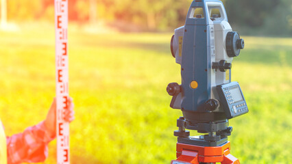 A man armed with a leveling rail makes topographic measurements, determining the height of the object. The device is mounted on a tripod surrounded by a grass carpet