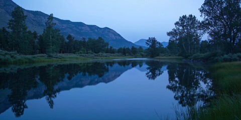 Sticker - A serene mountain lake with a perfect reflection of the surrounding trees under a blue sky.