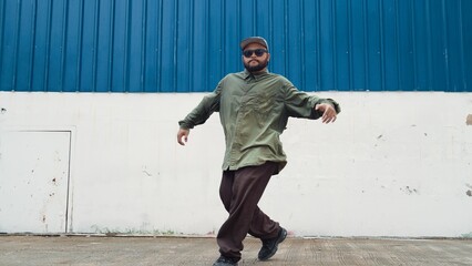 Hipster dancing b-boy foot step at street with blue wall. Asian break dancer practice street dance while stretch arms. Hip hop choreographer perform energetic dance. Outdoor sport 2024. Hiphop.