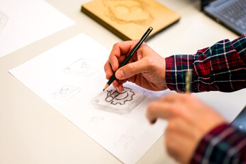 A close-up photo of a person's hands drawing a design on a piece of paper with a pencil