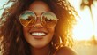 © familymedia - A radiant person with curly hair and sunglasses basks in the sunlight with a joyful smile, capturing the essence of positivity and summer freedom.