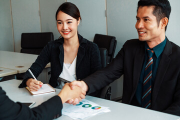 Business people agreement concept. Asian Businessman do handshake with another businessman in the office meeting room. Young Asian secretary lady sits beside him. uds