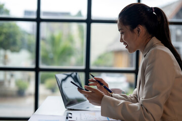 Wall Mural - A woman is sitting at a desk with a laptop and a cell phone