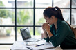 © apichat - A woman is sitting at a desk with a laptop and a calculator