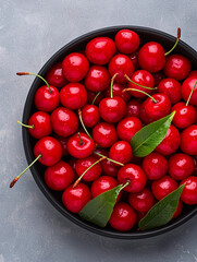 Wall Mural - Fresh and vibrant red cherries in black bowl, showcasing their glossy surface and green leaves, perfect for adding burst of color and flavor to any dish