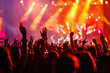 © oksa_studio - concert scene with enthusiastic fans raising their hands amidst colorful stage lights.