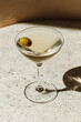 © Helen - Classic martini with olive served in a cocktail glass on a marble surface. Minimalist cocktail photography with strong shadows. Elegant drink concept.