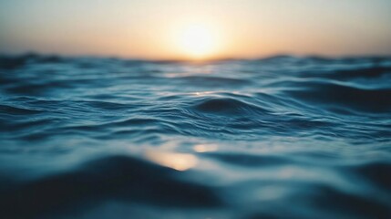 Closeup of rippling blue water with a blurred sunset in the background.