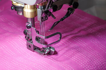 Poster - A sewing machine is in use on a pink fabric. The machine is in the process of sewing a piece of fabric