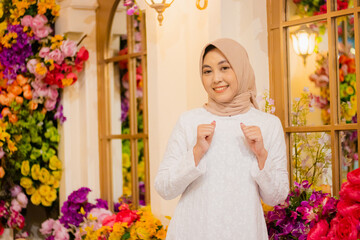 adult indonesia woman hijab wearing long white dress muslim cheerful to camera hands dancing among flower decoration in luxury restaurant. for fashion, beauty, lifestyle content