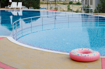 A large swimming pool filled with clear clean water at the edge of which lies a beautiful brightly colored inflatable swimming lap.