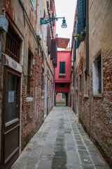  narrow street in the old town in Venice, Italy with red house 