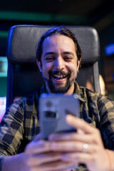 Cheerful male individual grasping his mobile device, chatting online with friends and family. Excited young man surfing the net on his cell phone, looking at funny content on social media.