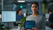 © Kateryna - A young female software developer standing at her workstation, holding a digital tablet with coding apps displayed on the screen. She gazes at the camera with a focused and determi
