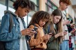 © miss irine - Multiracial group of teenagers using cell phones in school setting. Students engrossed in digital lives, attention focused on mobile apps, social media, texting. Four young people, different styles,