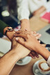 © SometimesNever/peopleimages.com - Collaboration, hands and unity with business people in coffee shop together for solidarity or support. Huddle, motivation and success with design employee group in cafe from above for teamwork