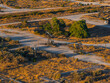 © Aerial Film Studio - Aerial perspective of an oil field in California's desert, featuring pumpjacks and dirt roads amidst sparse vegetation and arid terrain.