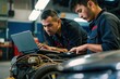 © miss irine - Two mechanics in noisy garage work together on car diagnostic. One mechanic uses laptop, examining engine parts, colleague checks electronic data. Teamwork in auto repair shop, cooperation in garage.
