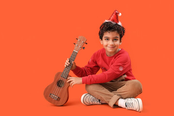 Canvas Print - Cute little boy in Santa hat playing guitar on orange background