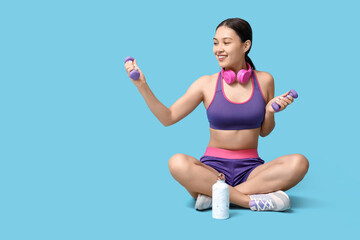 Poster - Young woman in sportswear and with dumbbells sitting against blue background