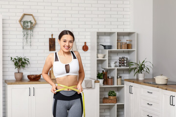 Sticker - Young woman measuring her waist in kitchen. Weight loss concept