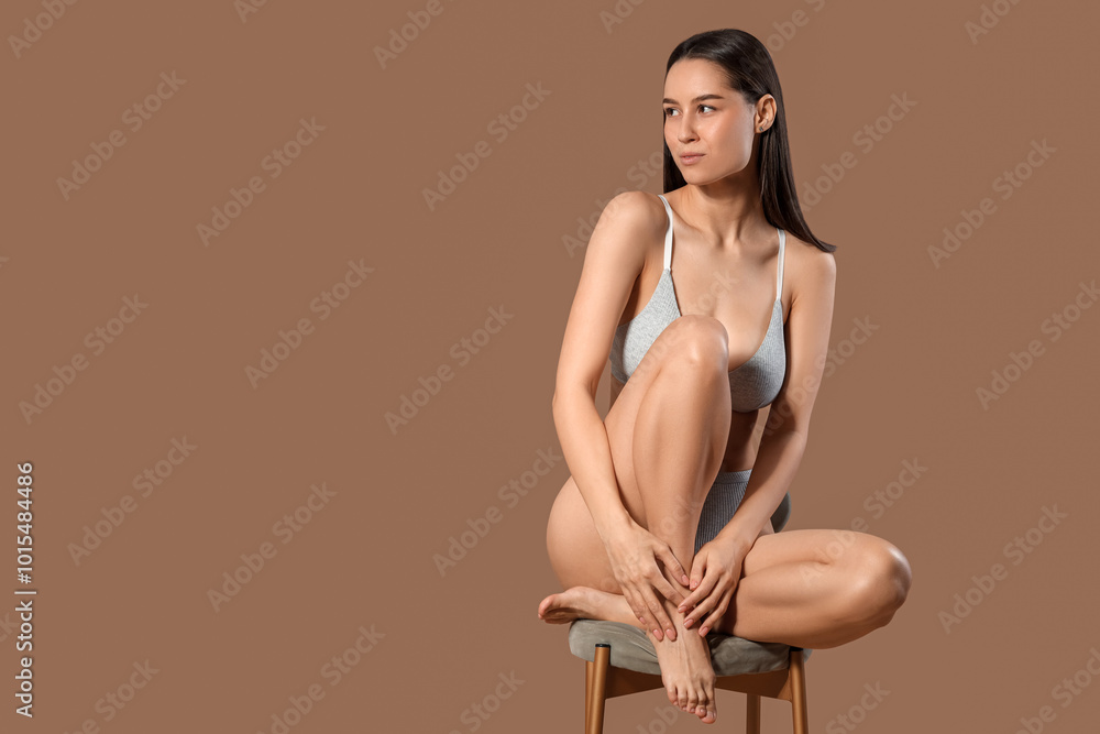 Slim young woman in cotton underwear sitting on chair against brown background