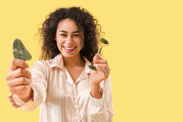 Poster - Young African-American woman with facial massage tools on yellow background