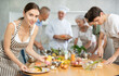 © JackF - Positive young woman attendee of cooking course decorating meal made of salmon fish together with others