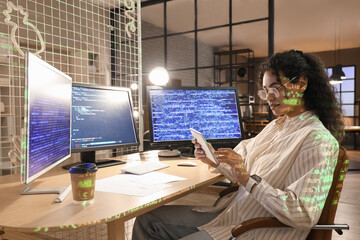 Wall Mural - Female African-American programmer with tablet computer working in office at night