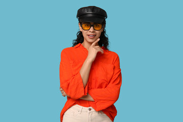 Poster - Stylish African-American woman wearing sunglasses and hat on blue background