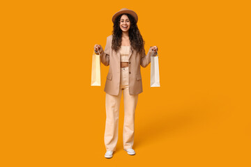 Stylish African-American woman with shopping bags on yellow background