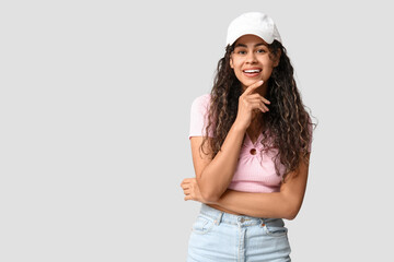 Poster - Stylish African-American woman wearing top, jeans and cap on light background