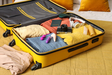 Open suitcase with clothes, sex toys, cosmetics and photo camera on bed