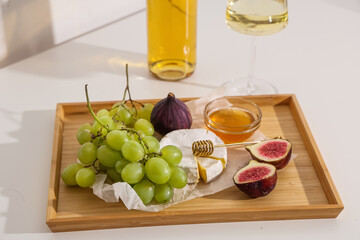 Wooden board with sweet ripe grapes, figs, camembert cheese, honey and bottle of wine on white background