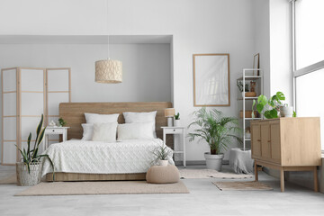 Poster - Beautiful interior of light bedroom with wooden chest of drawers, window, houseplants and bed